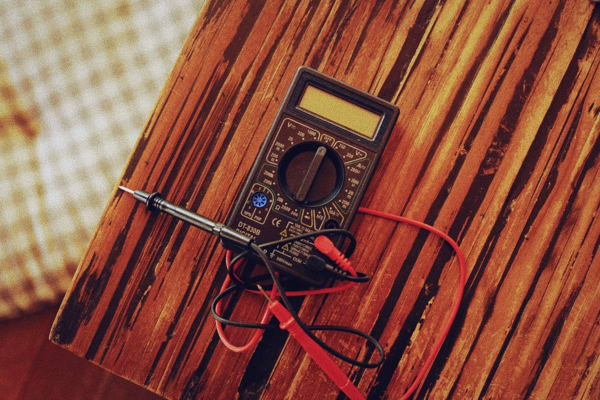 Multimètre digital posé sur un établi en bois, pointes de touche et cordons de mesure déroulés.