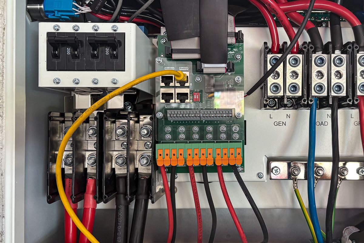 Intérieur d'une armoire électrique ouverte : disjoncteurs, bornier à ressort orange sur carte électronique, câbles rouges et noirs.